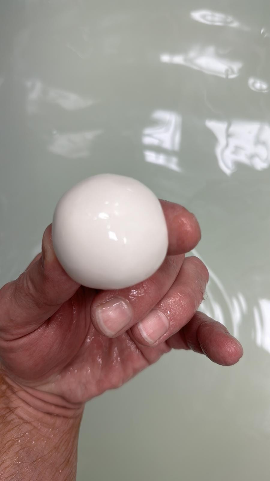 Boule de mozzarella fraîche et brillante tenue à la main au-dessus de la saumure.